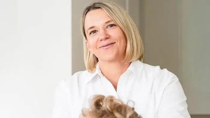 Die Ärztin in weißem Hemd lacht in die Kamera, davor ist ein Junge mit blonden Haaren zu sehen