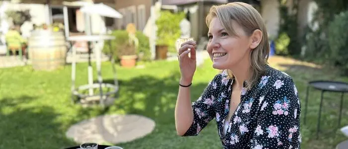 Eine Frau in sommerlicher Kleidung sitzt in einem Garten und spricht lächelnd