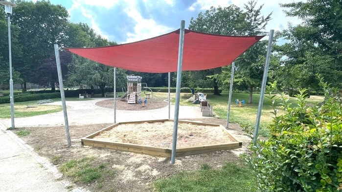 Zu sehen ist eine sechseckige Sandkiste mit einer roten Überdachung 