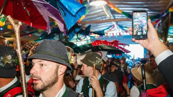 Männer mit Regenschirmen ziehen in ein Festzelt ein.