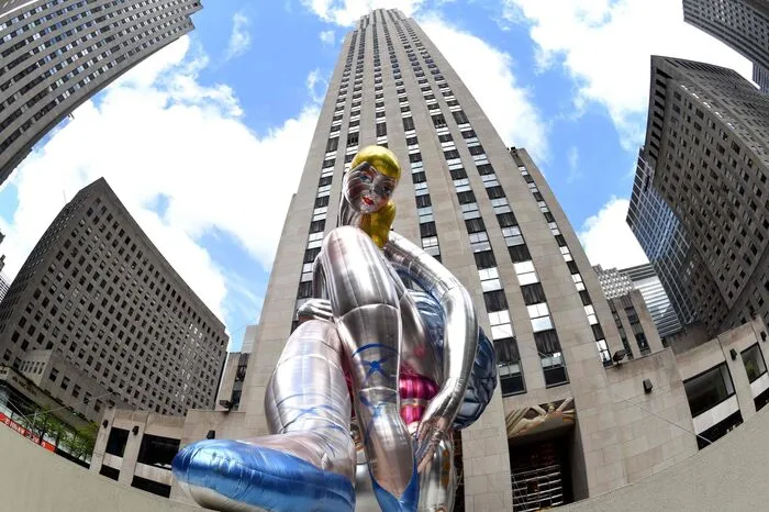 Die silber-metallische Ballett-Tänzerin mit blonden Haaren, blauen Augen und einem roten Mund lächelt von oben auf die goldenen Prometheus-Statue hinab, die vor dem Rockefeller Center in Manhattan steht. Die Installation soll auf den Monat der vermissten Kinder aufmerksam machen, der im Mai begangen wird.