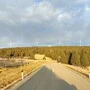 Sechs Windräder am Horizont, davor Straße, bewaldeter Hügel