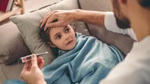 Sick little girl covered in blanket is lying on couch while her father is taking her temperature
