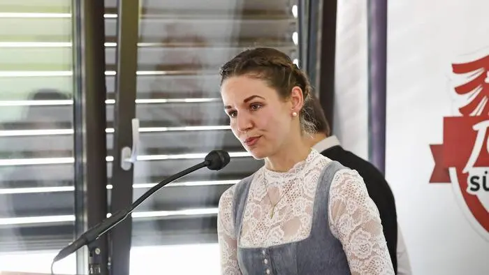 Melanie Mair spricht in ein Mikrofon. Hinter ihr ist ein gekipptes Fenster mit heruntergelassener Jalousie.