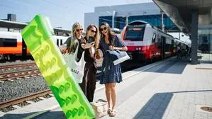Drei junge Damen machen ein Selfie am Bahnhof mit Luftmatratze