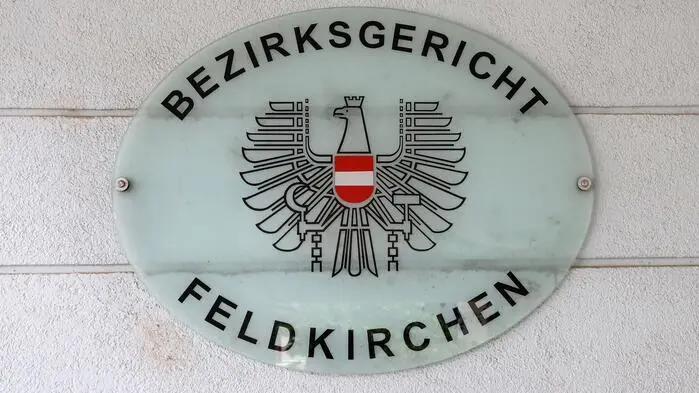 Ein Schild hängt an einer Wand. Darauf steht: „Bezirksgericht Feldkirchen“.