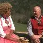 Ein Mann und eine Frau, beide in Tracht, sitzen auf einem Strohballen und unterhalten sich 