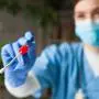 Female caucasian NHS doctor holding a swab collection stick, nasal and oral specimen swabbing in doctor's office, patient PCR testing procedure appointment, Coronavirus COVID-19 global pandemic crisis