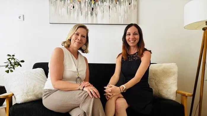 Zwei Frauen sitzen auf einem Sofa und lächeln in die Kamera