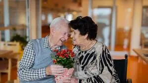 Ein älterer Mann übergibt einer älteren Frau Blumen und lächelt sie an