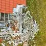 Aerial view on damaged red single house roof after strong wind or explosion. Hole in the rooftop and floor. Rubble on the ground.