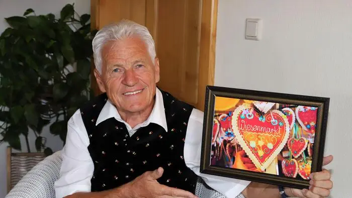 Ein Herr, Mitte 70, hält ein Foto von einem Lebkuchenherz in den Händen und lächelt in die Kamera.