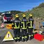Drei Feuerwehrleute stehen in Einsatzkleidung an einer Einsatzstelle.