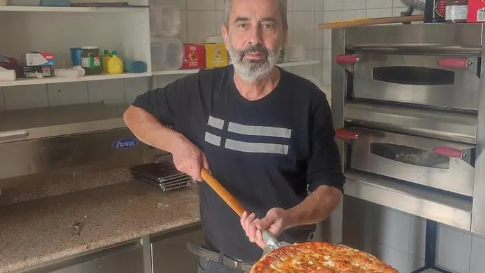 Ein Mann mit grauen Haaren und Bart hält eine Pizza auf einer Pizzaschaufel