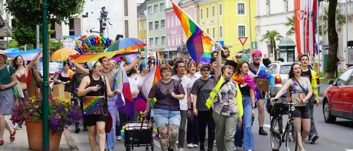 Mehrere Personen der LGBTQIA+-Community ziehen durch die Straßen und halten Regenbogen-Fahnen hoch
