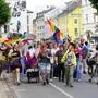 Mehrere Personen der LGBTQIA+-Community ziehen durch die Straßen und halten Regenbogen-Fahnen hoch