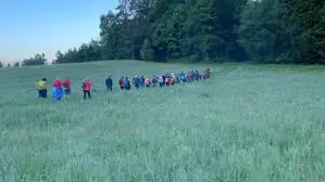 Eine grüne Wiese, blauer Himmel und mehrere Menschen in einer Reihe, die bergauf gehen
