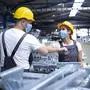 Workers greeting each other with elbow bump due to global corona virus pandemic and danger of infection. Employees standing in factory wearing protection mask.