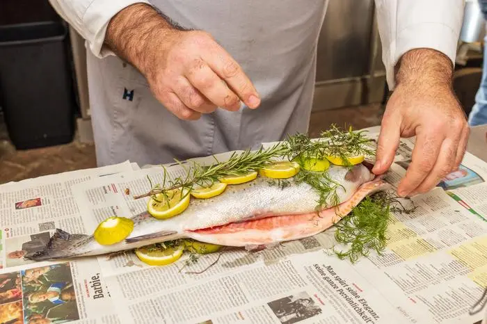 Die Lachsforelle wird in einem Bett aus Kräutern und Zitronenscheiben mit Zeitungspapier eingewickelt