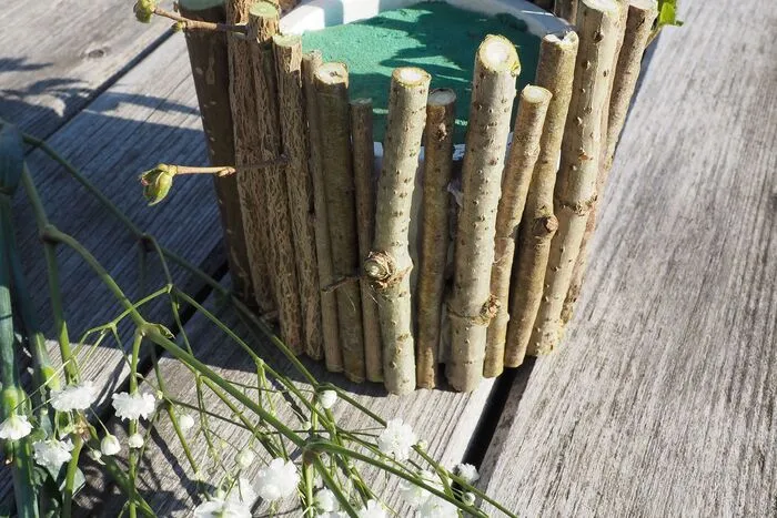 Danach die kleinen Hölzer stückweise mit der Heißklebepistole nebeneinander am Blumentopf ankleben.
