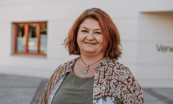 Das Foto zeigt Doris Dirnberger im Freien auf einem Platz. Im Hintergrund ist unscharf die Außenmauer eines Gebäudes zu sehen.