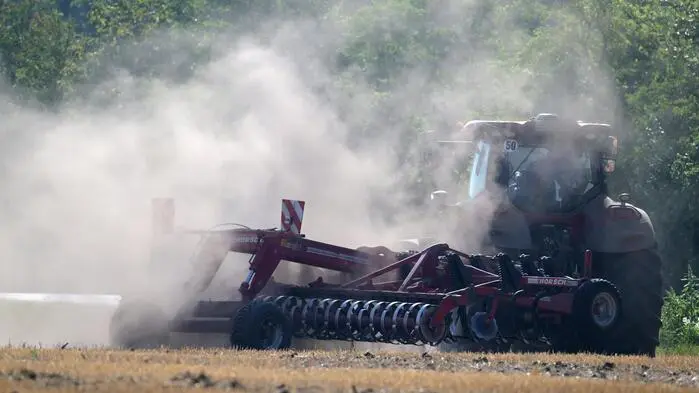 Ein Traktor pflügt durch ein vertrocknetes Feld, darüber bildet sich eine dichte Staubwolke