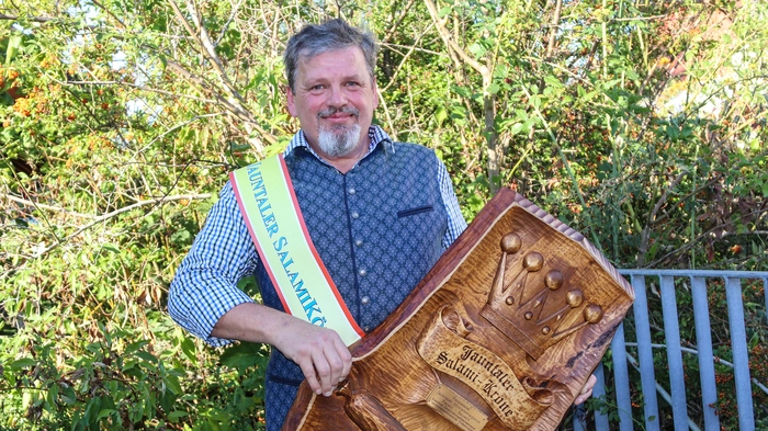 Ein Mann mit grauen Haaren und Bart hält eine Auszeichnung in der Hand
