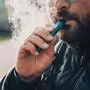Man smokes new Vape Pod System, inhales and exhales vapor of electronic cigarette, vaping concept, selective focus, toned