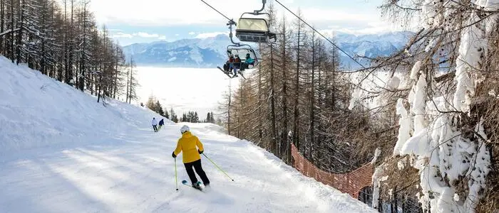 Ein Skifahrer auf einer Piste, darüber fährt ein Sessellift.