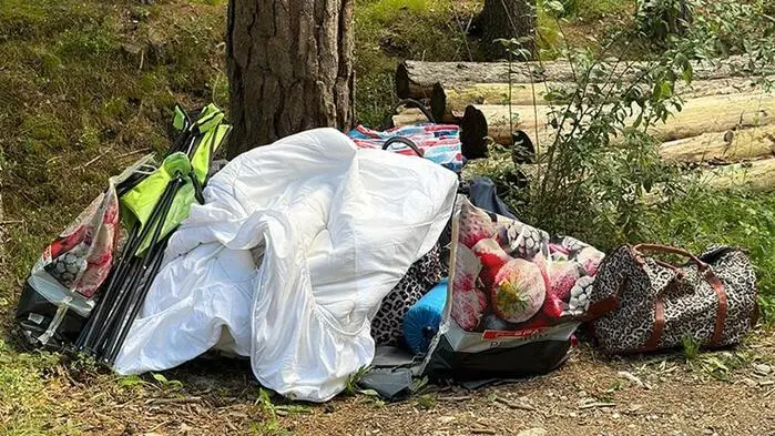 In einem Waldstück liegen Plastiksäcke, Taschen, Decken und Leintücher auf dem Boden verteilt