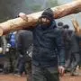 A migrant carries a tree trunk delivered by the Belarusian officials in a camp on the Belarusian-Polish border in the Grodno region on November 14, 2021. - Dozens of migrants have been detained after crossing into Poland from Belarus, Warsaw said on November 14, warning of a possible larger breakthrough ahead of an EU meeting to widen sanctions on Belarus. (Photo by Oksana MANCHUK / BELTA / AFP) / Belarus OUT