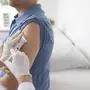 Doctor injecting vaccine in arm of male patient in hospital
