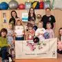 Mehrere Kinder und erwachsene Frauen haben sich für ein Gruppenbild platziert und halten Handpuppen und ein Plakat in die Kamera