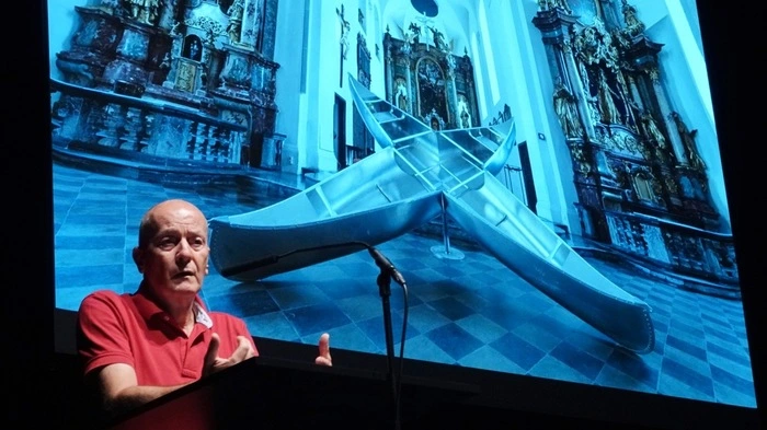 Erwin Lackner mit einem Bild seiner Skulptur "Kreuzfahrt", die derzeit im Rahmen der Ausstellung „maßlosmittellos“ in der Stadtgalerie im Kunsthaus Weiz zu sehen ist. Lackner zeigt sich in seiner Arbeit sowohl als Kritiker, als auch als satirischer Beobachter.