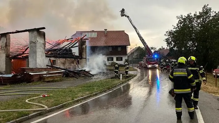 Man sieht ein stark niedergebranntes Gebäude, daneben Feuerwehrleute