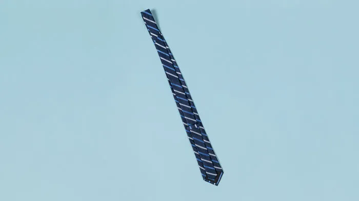 1. Die Krawatte mit der Vorderseite auf einen glatten Untergrund legen. Mittig, von oben nach unten, falten und die Rückseite durch die Schlaufe hinten auf der Krawatte ziehen, damit nichts mehr verrutschen kann.