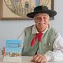 Horst Krauland mit Kochbuch vor dem Gottscheer Wappen. Die Gottscheer Tracht wurde von den slawischen Nachbarn, den Weißkrainern, beeinflusst 