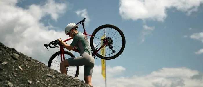 Ein Radfahrer trägt ein Fahrrad einen Schotterhügel hinauf