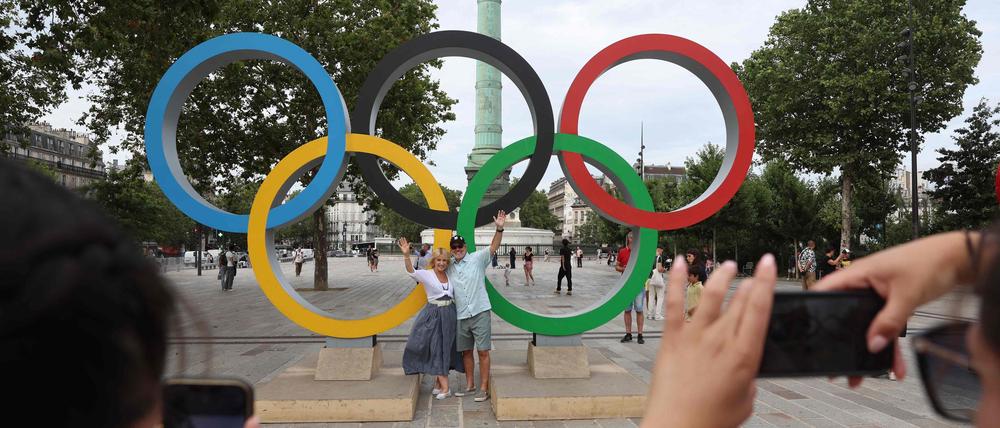 People pose for photos in front of the Olympic rings near the July Column in Paris on July 25, 2024, a day ahead of the opening ceremony of the Paris 2024 Olympic Games. (Photo by Emmanuel DUNAND / AFP)
