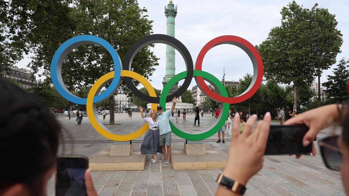 People pose for photos in front of the Olympic rings near the July Column in Paris on July 25, 2024, a day ahead of the opening ceremony of the Paris 2024 Olympic Games. (Photo by Emmanuel DUNAND / AFP)