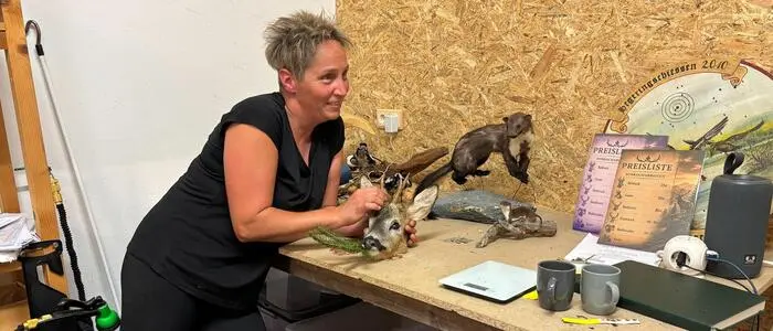 Eine blinde Frau lehnt über einen Arbeitstisch voller ausgestopfter Tiere