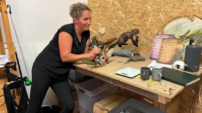 Eine blinde Frau lehnt über einen Arbeitstisch voller ausgestopfter Tiere