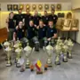 Neun Männer mit vielen Pokalen und Feuerwehrhelmen