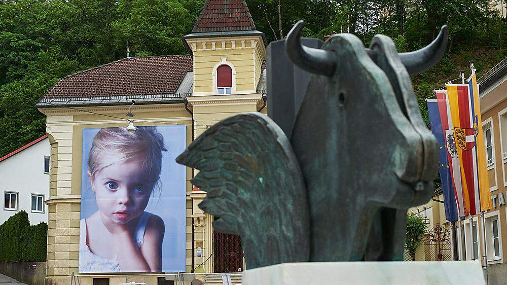Fassade mit einem Kinderporträt von Gottfried Helnwein am Hauptplatz von Bleiburg. Im Vordergrund: Kiki Kogelniks Freyungsbrunnen	