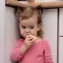 Cute adorable caucasian toddler girl eating tasty toasts from delicious bread at kitchen, looking down, portrait, hungry child, childhood concept.