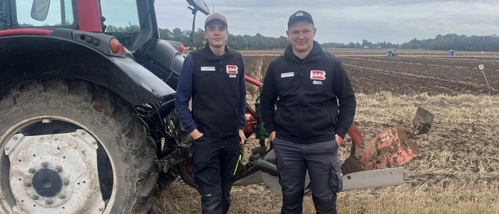 Zwei Schüler, gekleidet in schwarz, stehen neben einem Traktor
