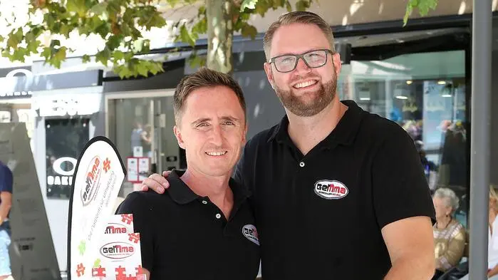 Zwei Männer in schwarzen Poloshirts lächeln in die Kamera