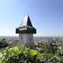 Das Bild zeigt den Grazer Uhrturm und einen Blick auf die Stadt.