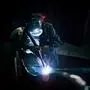 Industrial worker in protective clothing welding metal with welding torch