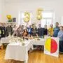 Rund 15 Menschen stehen hinter einem Tisch mit weißer Tischdecke und lächeln in die Kamera, über ihnen Ballons mit der Zahl 35